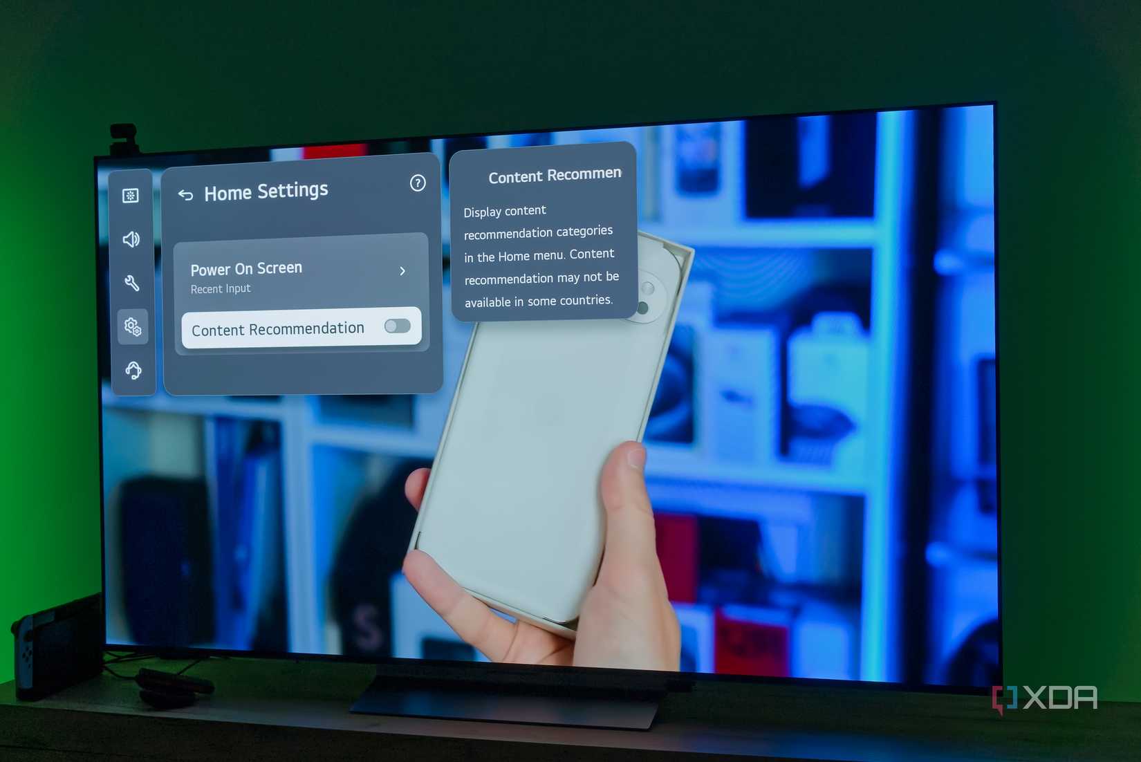 An LG TV displaying settings for the home screen over an image of a smartphone held in someone's hand
