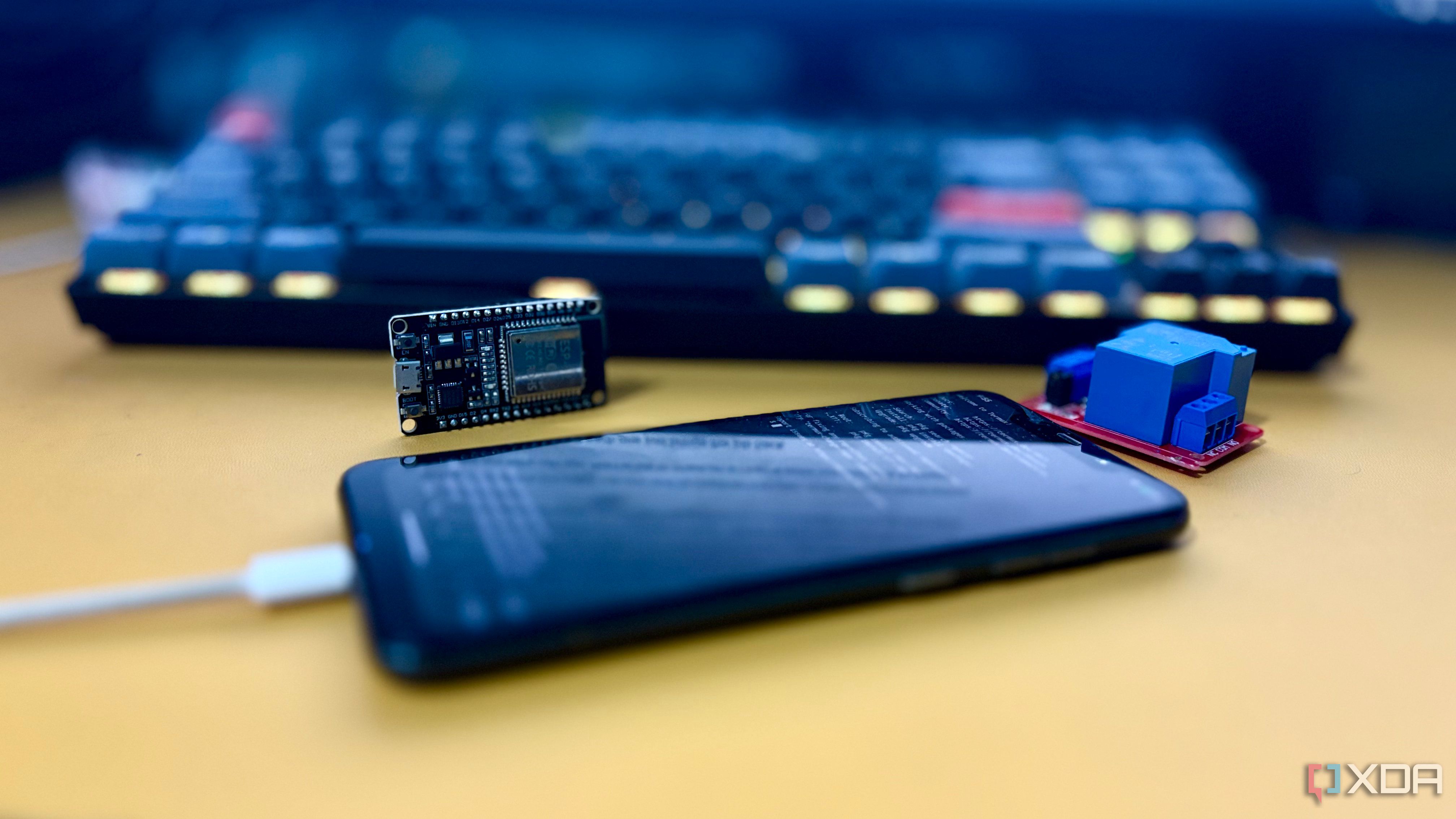 An old phone charging next to an ESP32 board and a relay module