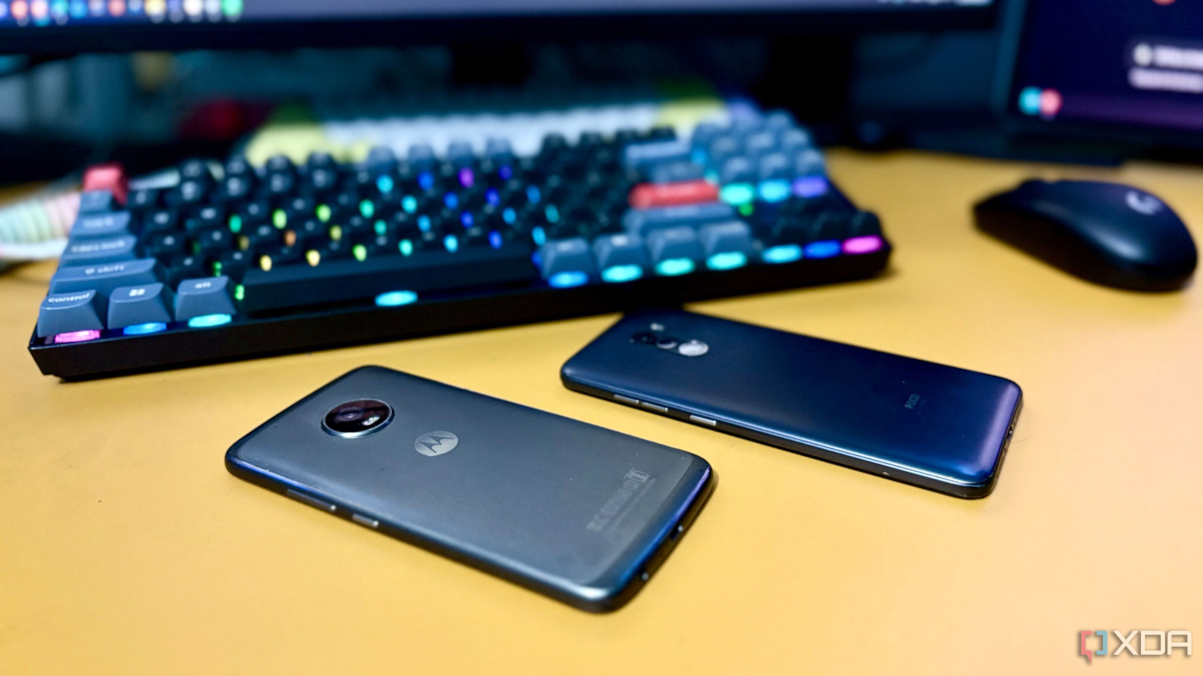 POCO F1 and Moto G5 Plus lying face-down on a desk next to a mechanical keyboard