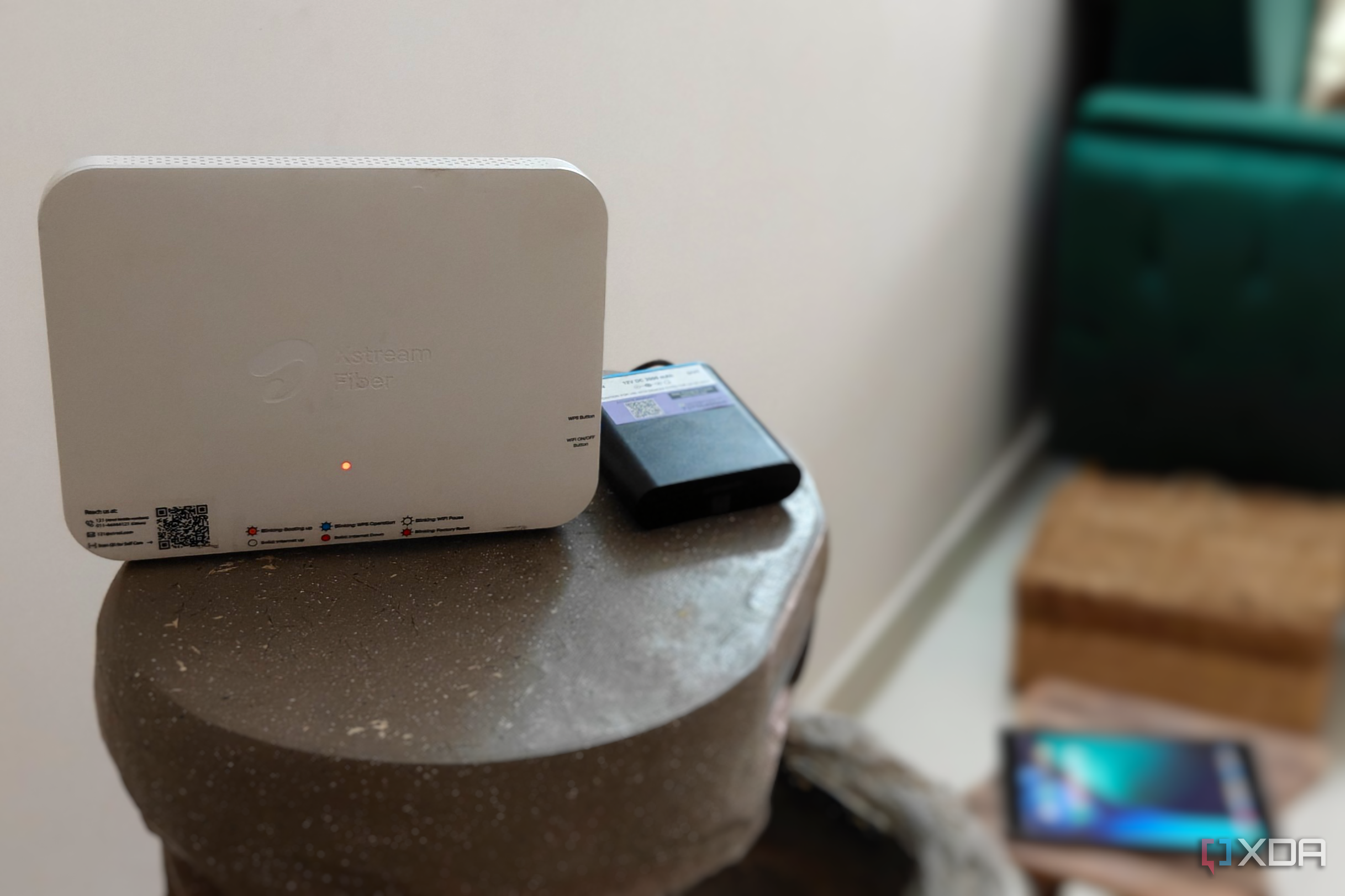 A white Wi-Fi router next to a mini UPS on a grey surface