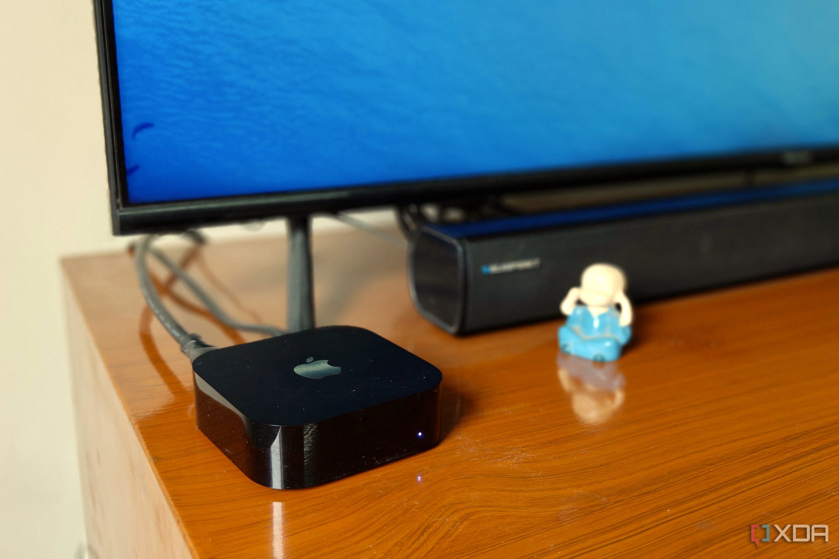Close-up of a black streaming box next to a soundbar and TV on a brown desk