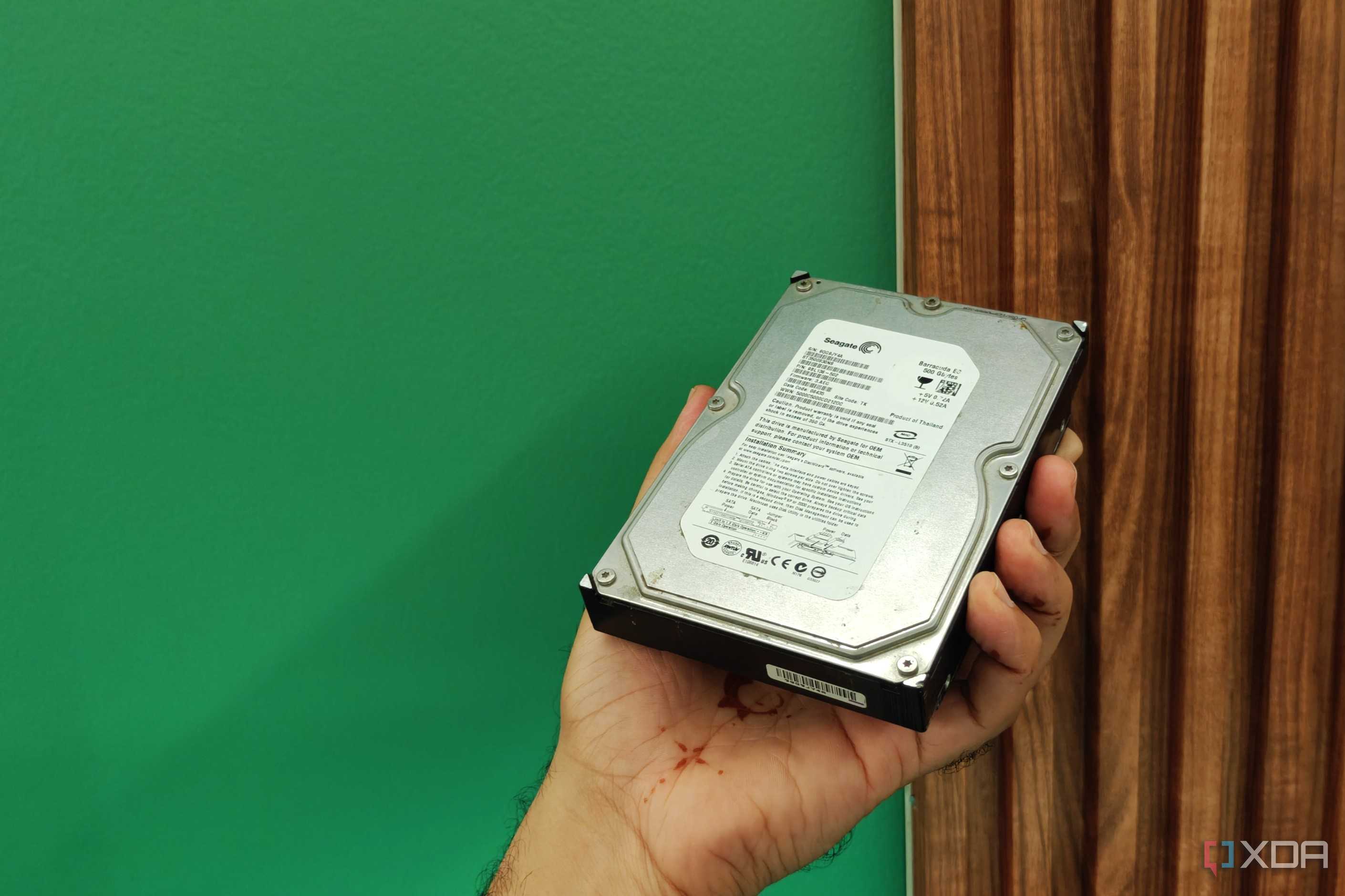 A hard drive held in a hand next to a green and brown background