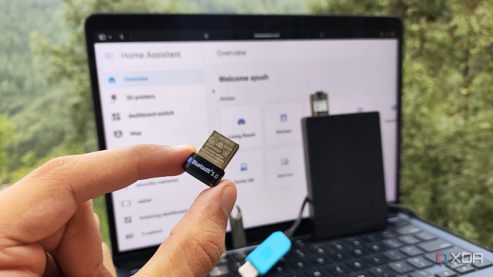 Человек держит Bluetooth-адаптер и USB-устройства на фоне веб-интерфейса Home Assistant