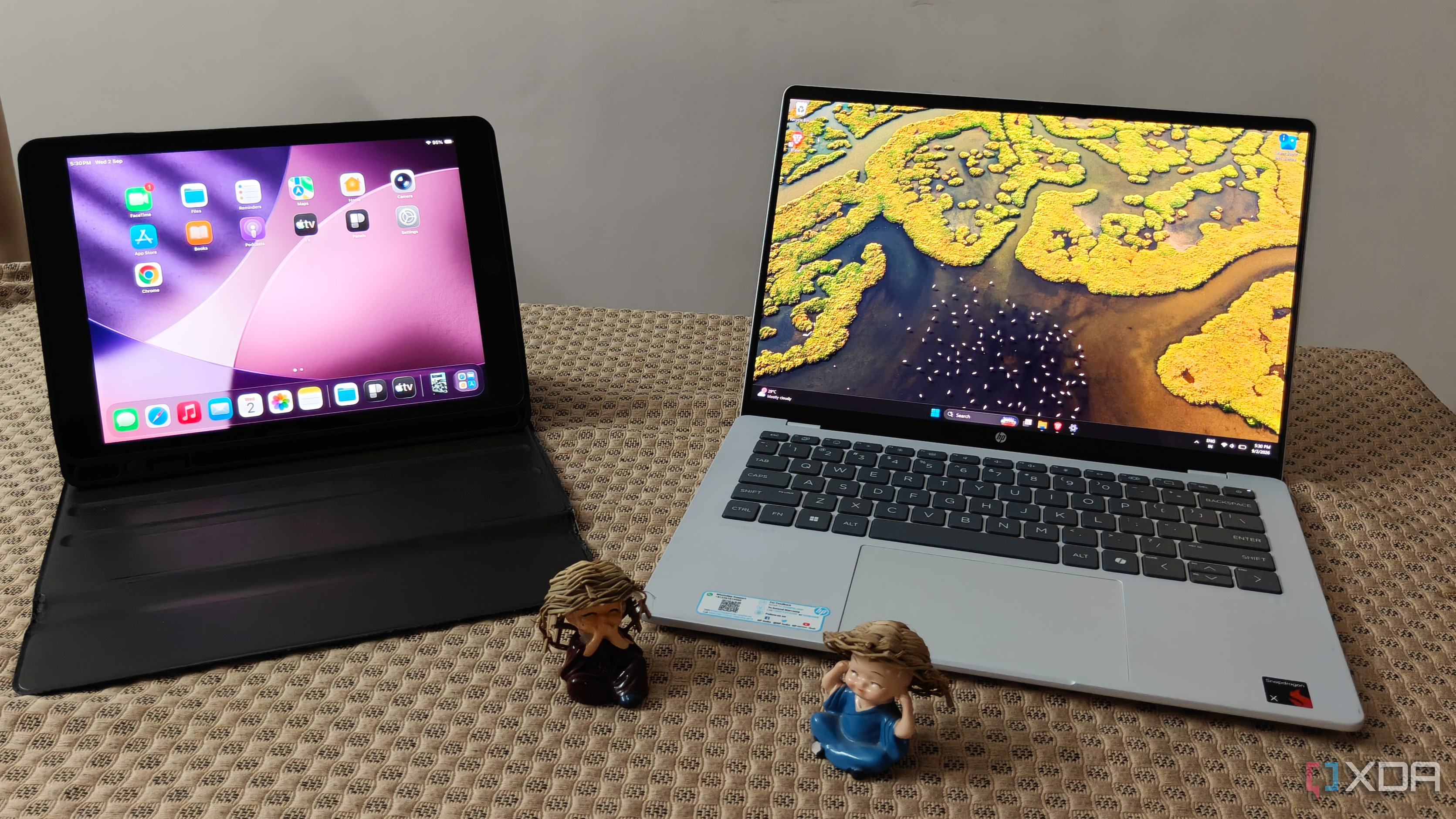 An iPad and a laptop with two figurines on a brown fabric