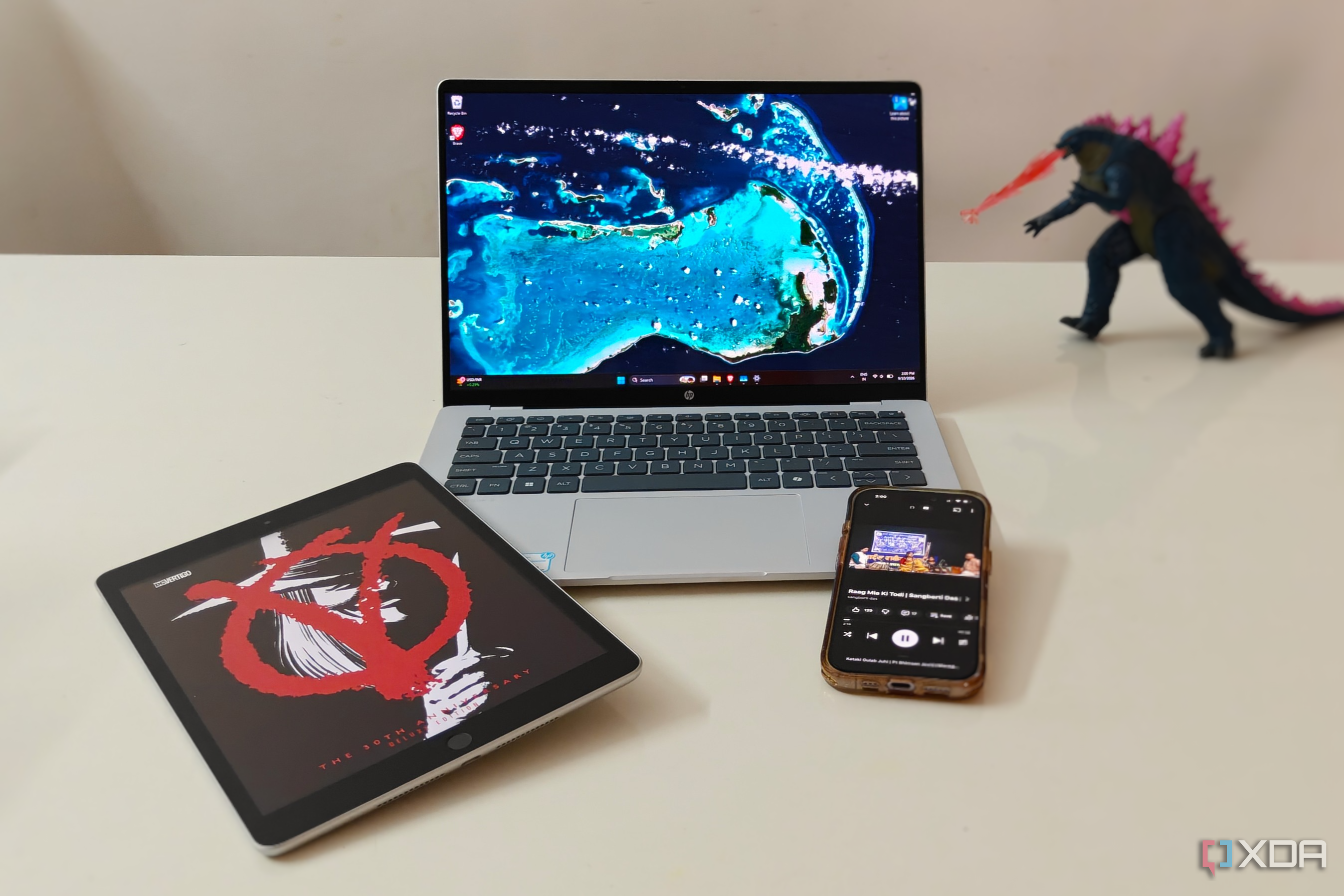 A laptop, iPad, and iPhone on a white desk with a figurine in the background