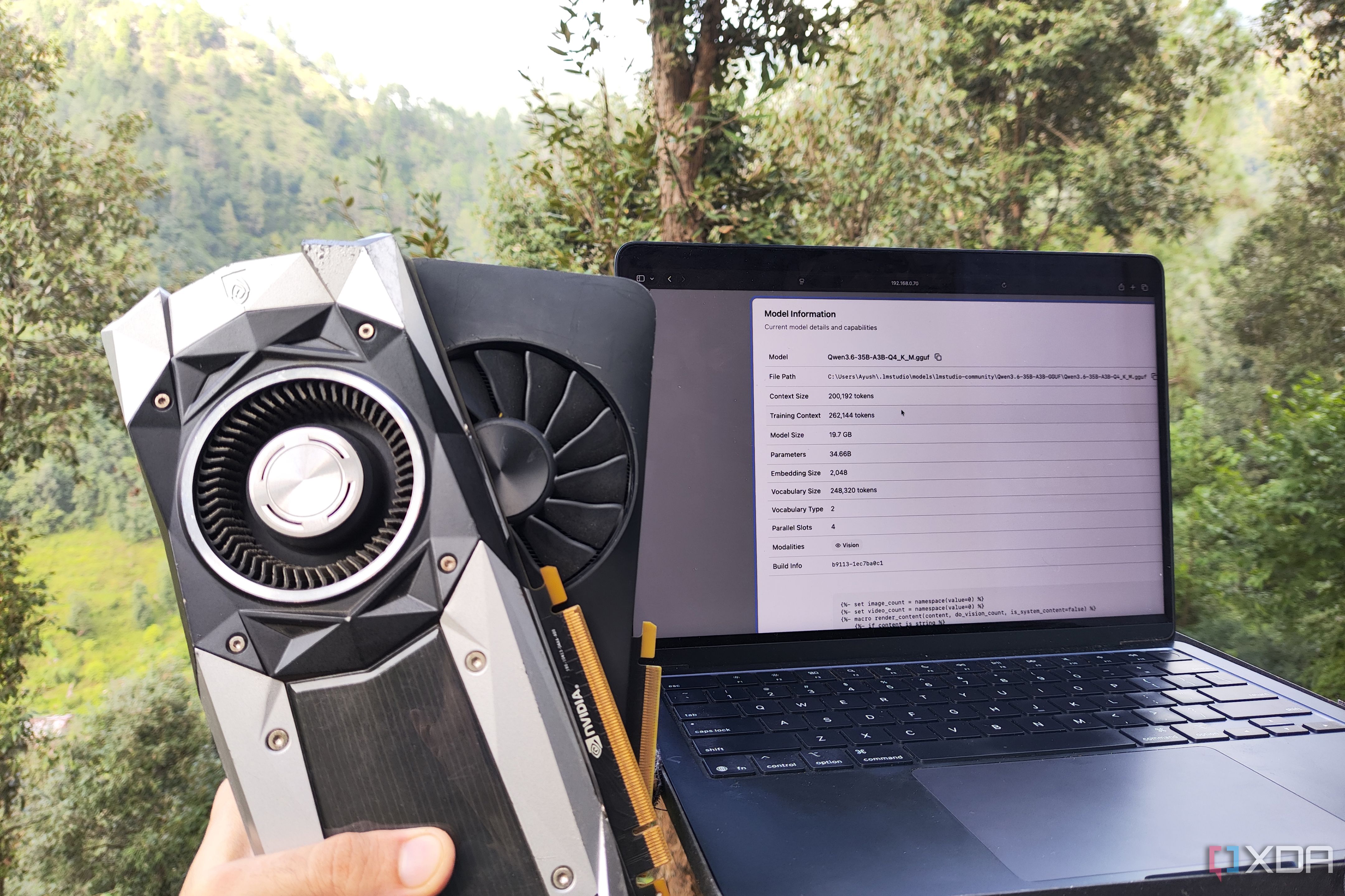 A person holding two GPUs next to a laptop with the llama.cpp web UI open