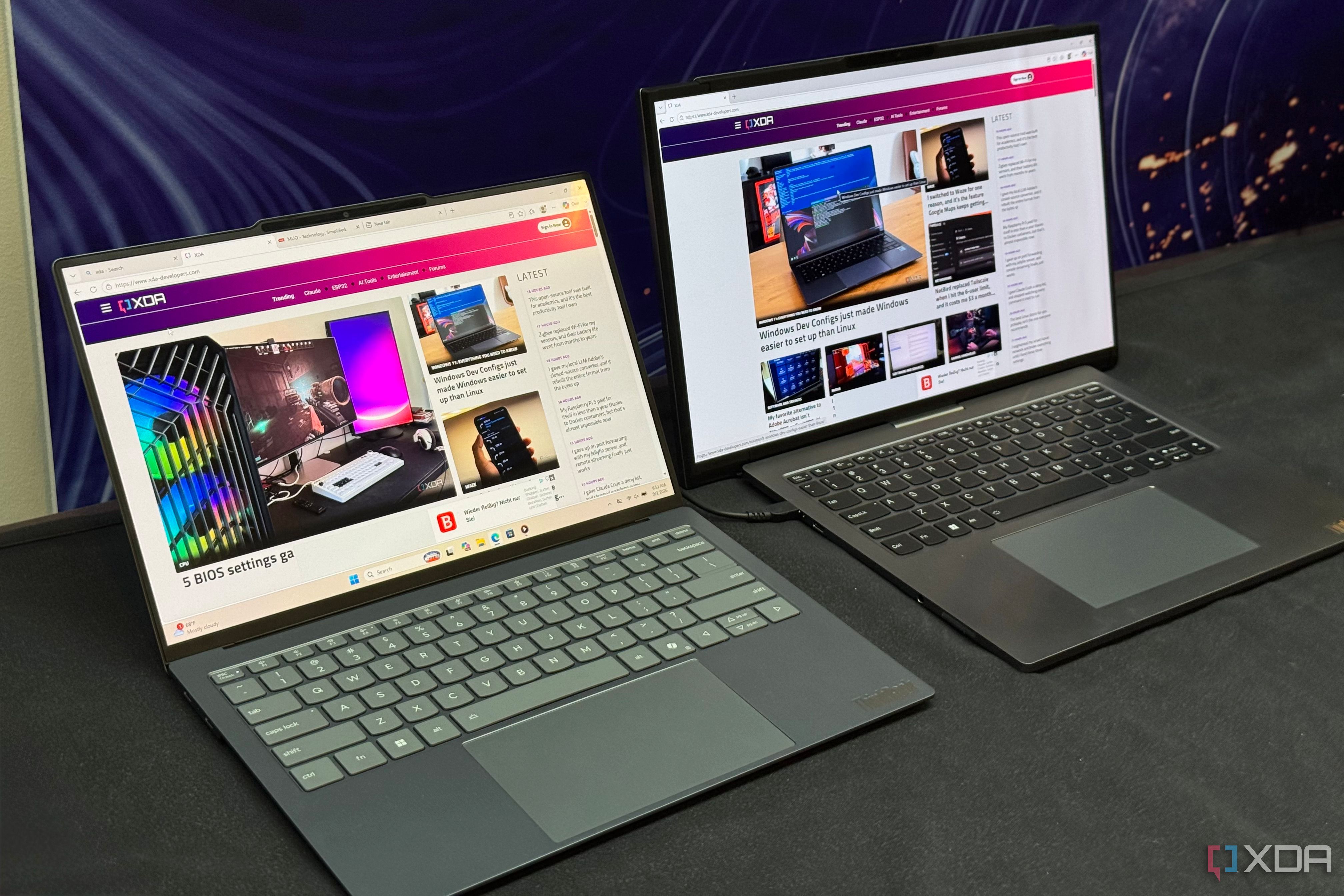 Pair of ThinkBook laptops angled on a booth table with XDA open on both screens