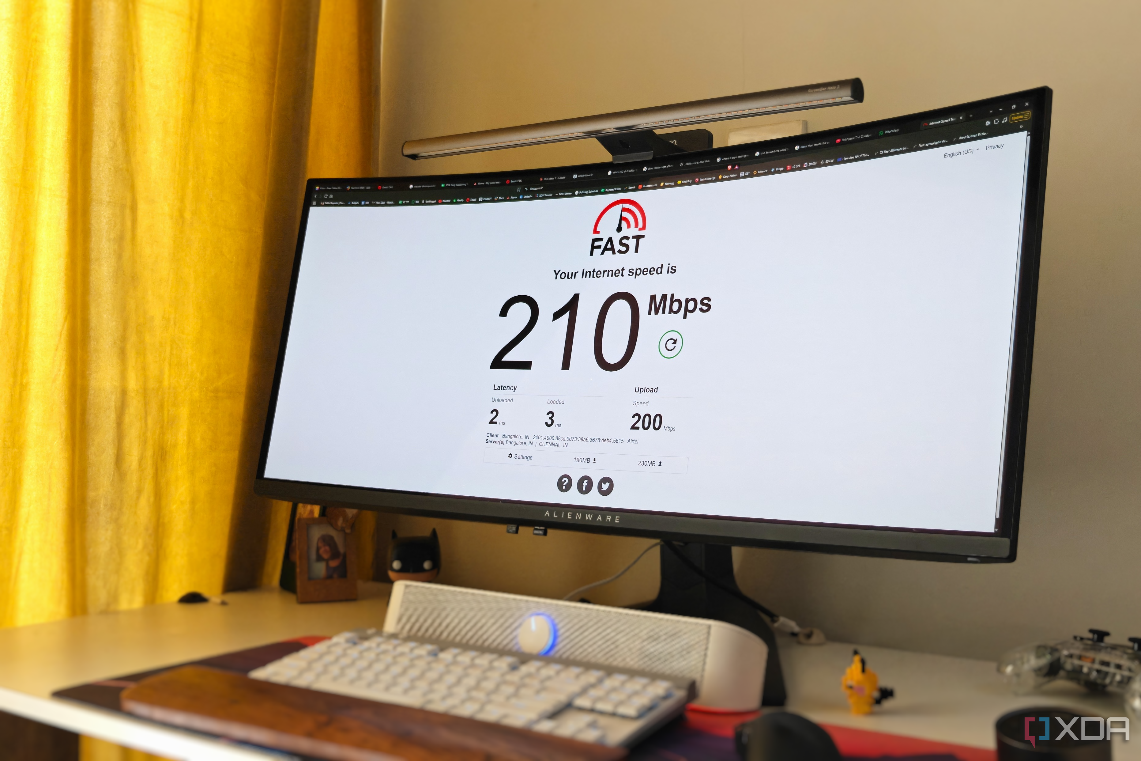 An ultrawide monitor on a desk next to a yellow curtain showing an internet speed test