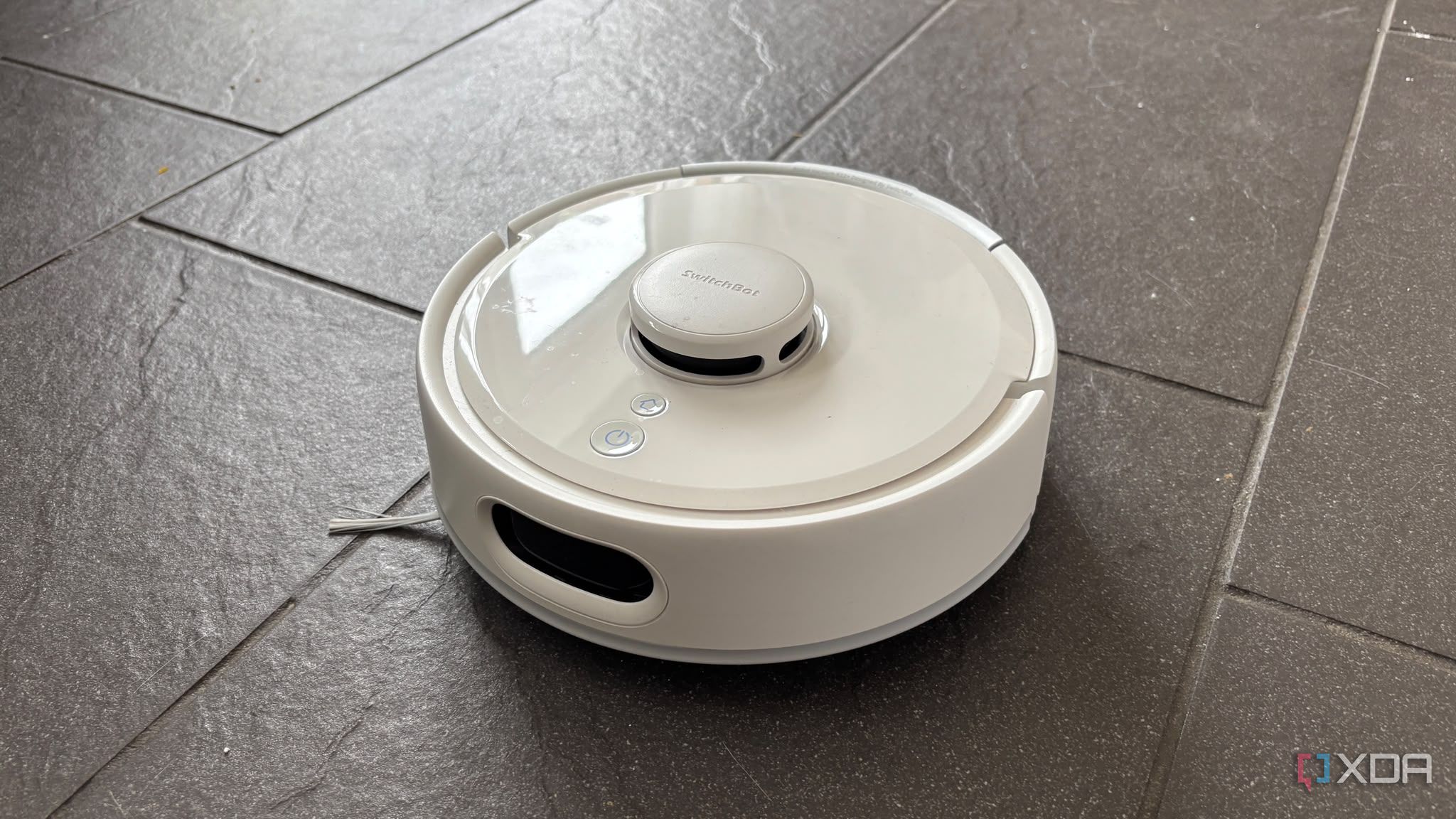 Switchbot smart robot vacuum being shown on a black floor away from dock
