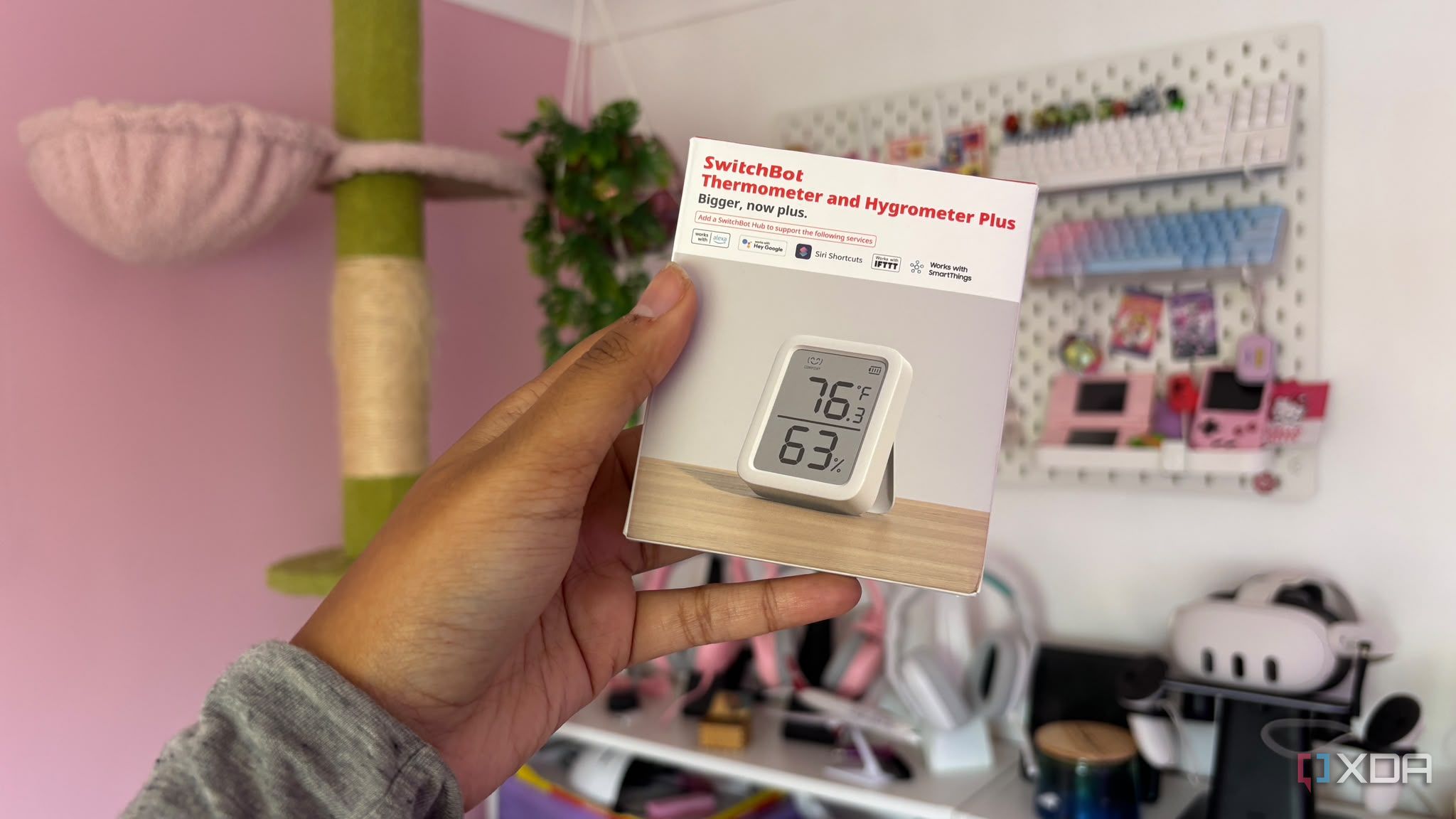 Switchbot temp and humidity sensor being held up against pink background