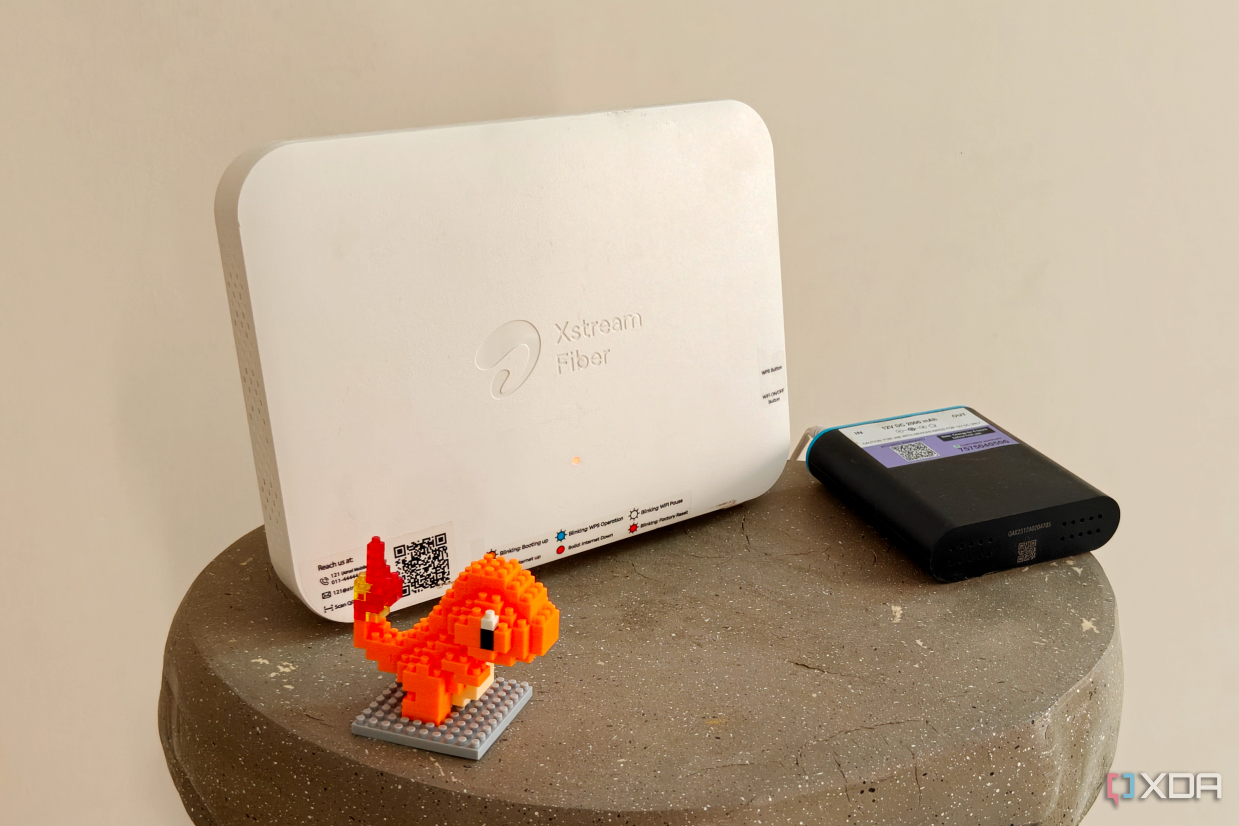 A white Wi-Fi router next to a black min UPS and an orange figurine