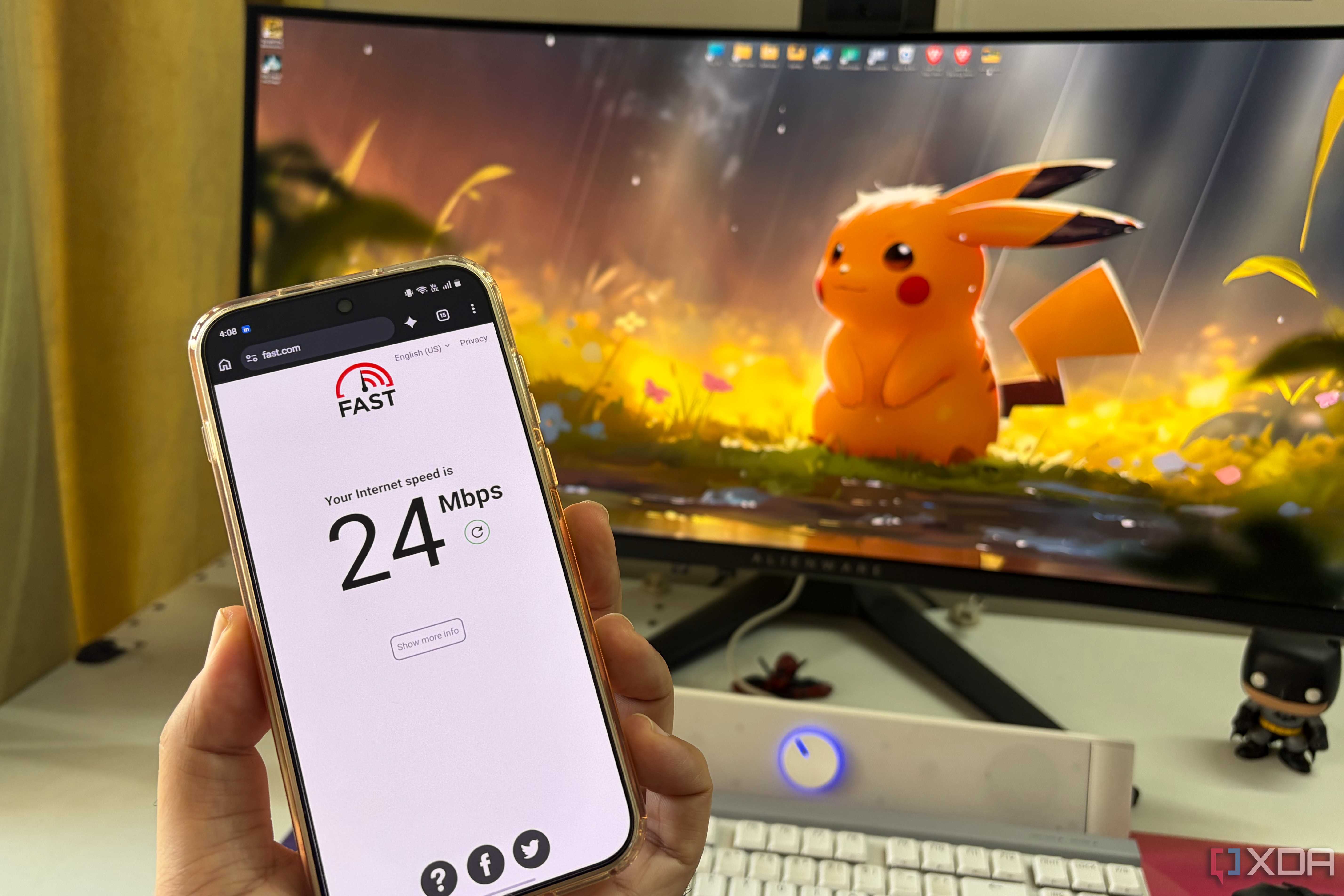 Close-up of a smartphone showing a Wi-Fi speed test with a PC setup in the background