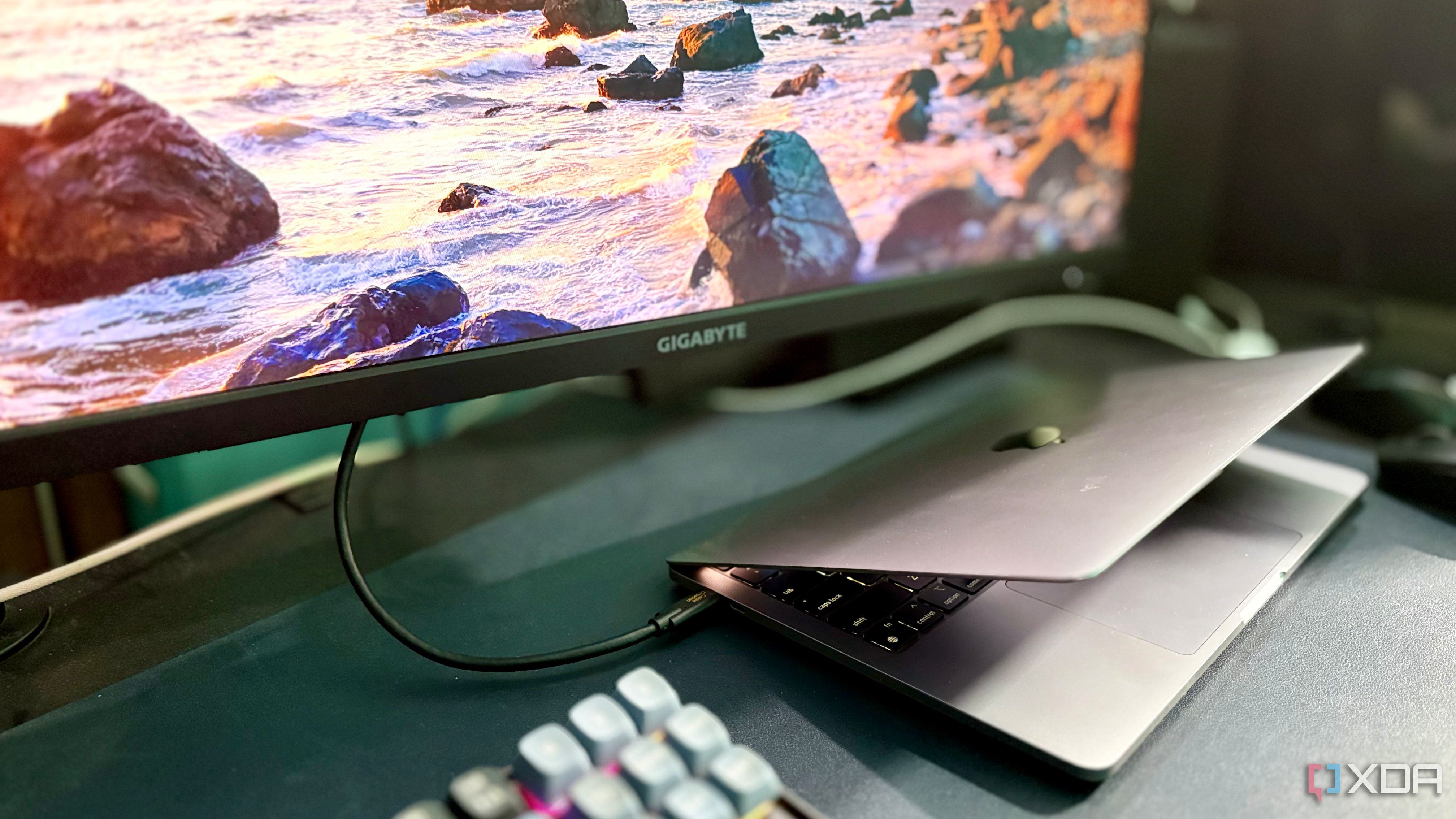 Black CableCreation cable running from a MacBook Pro to a Gigabyte monitor showing a coastal wallpaper