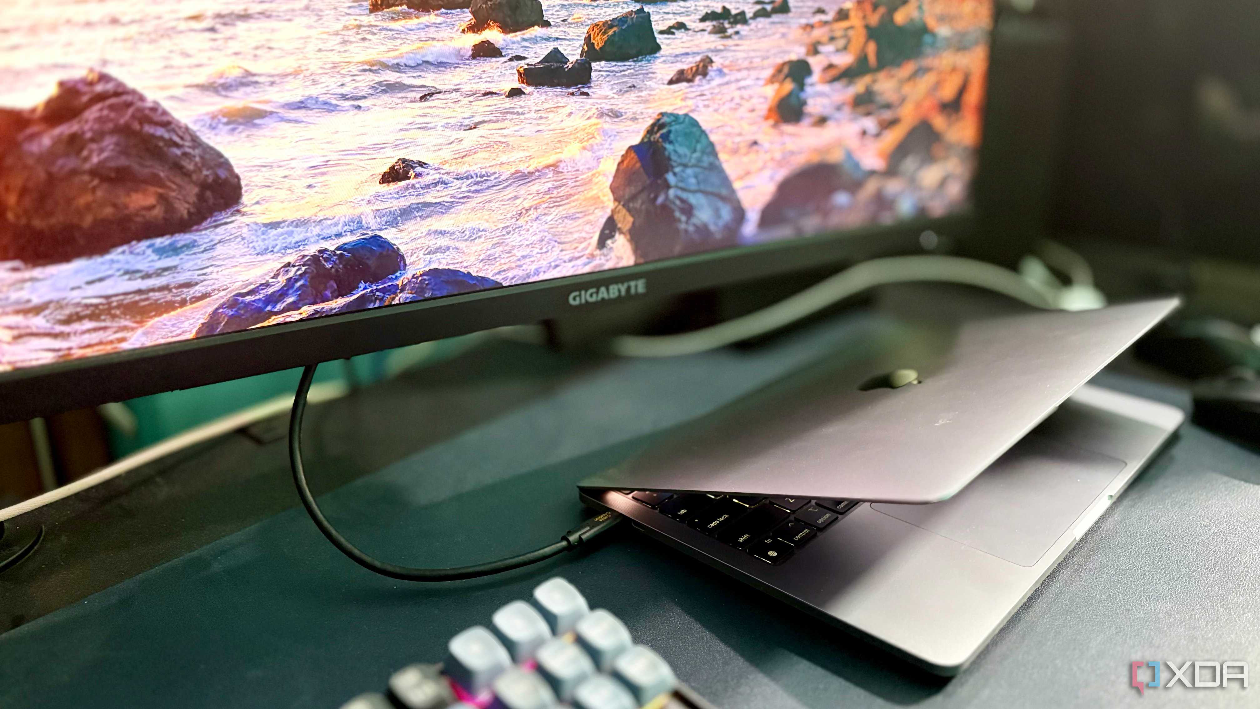 Black CableCreation cable running from a MacBook Pro to a Gigabyte monitor showing a coastal wallpaper