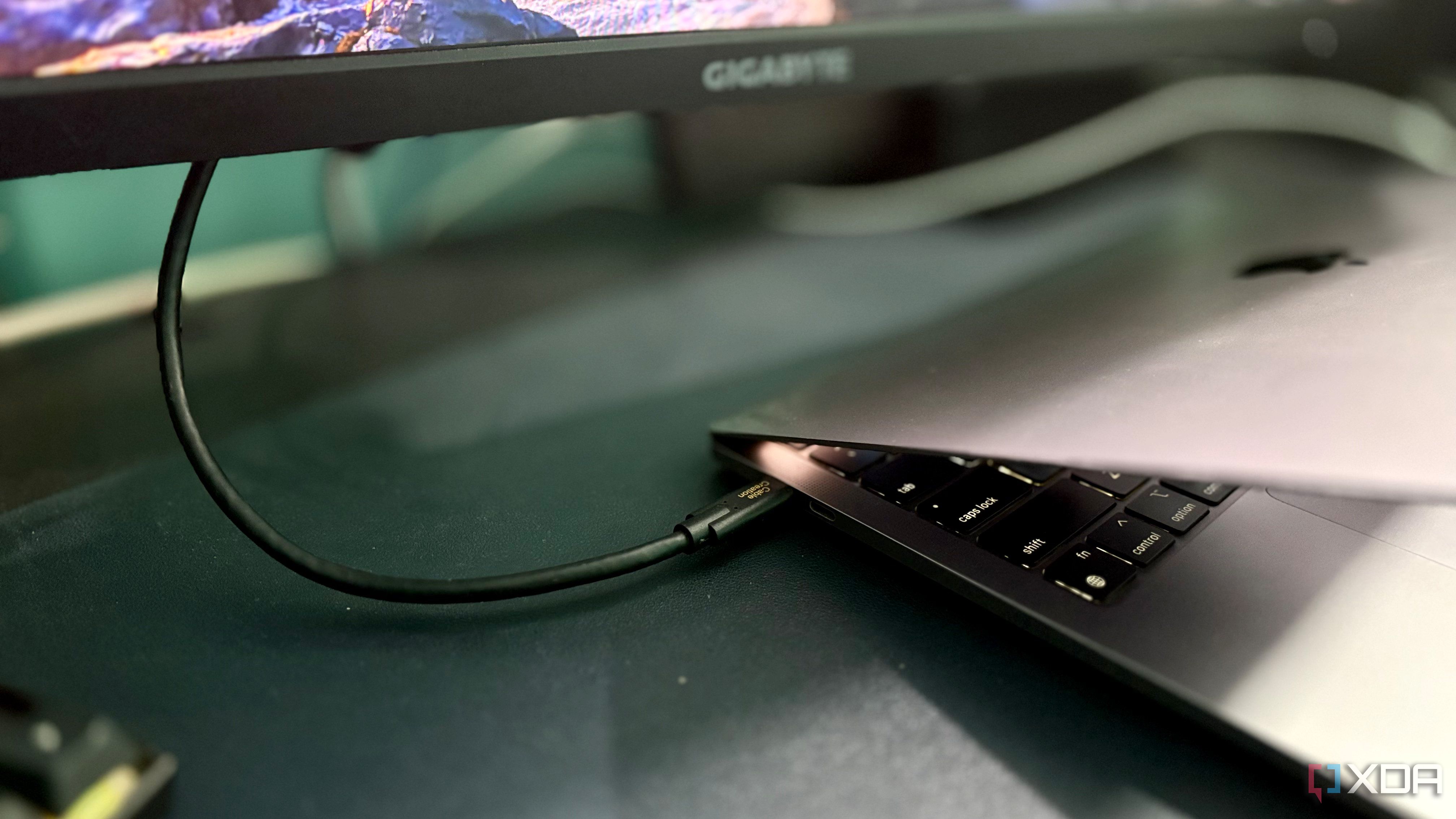 CableCreation USB-C connector plugged into the side port of a MacBook Pro below a Gigabyte monitor