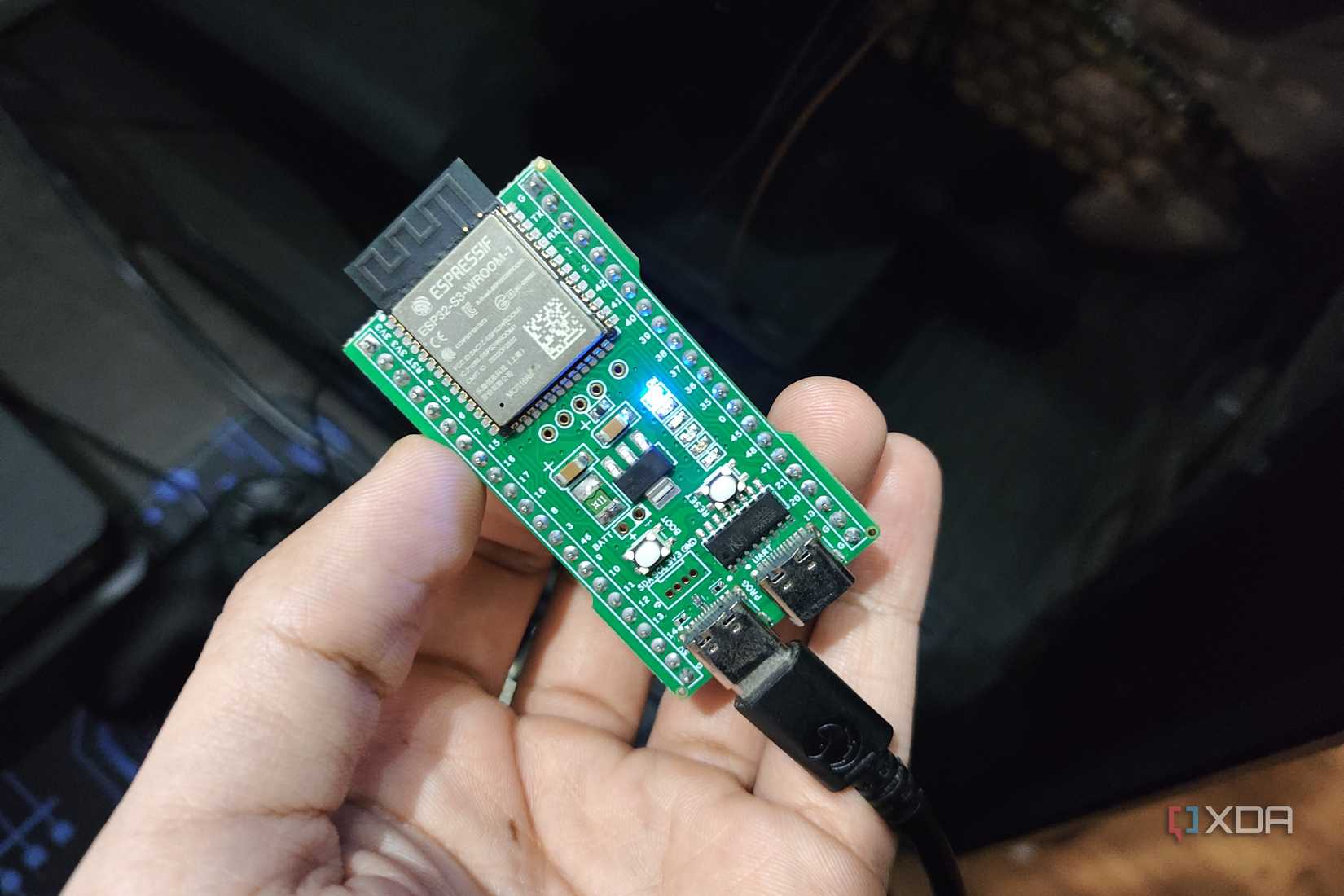 Человек держит плату ESP32-S3, подключенную к персональному компьютеру