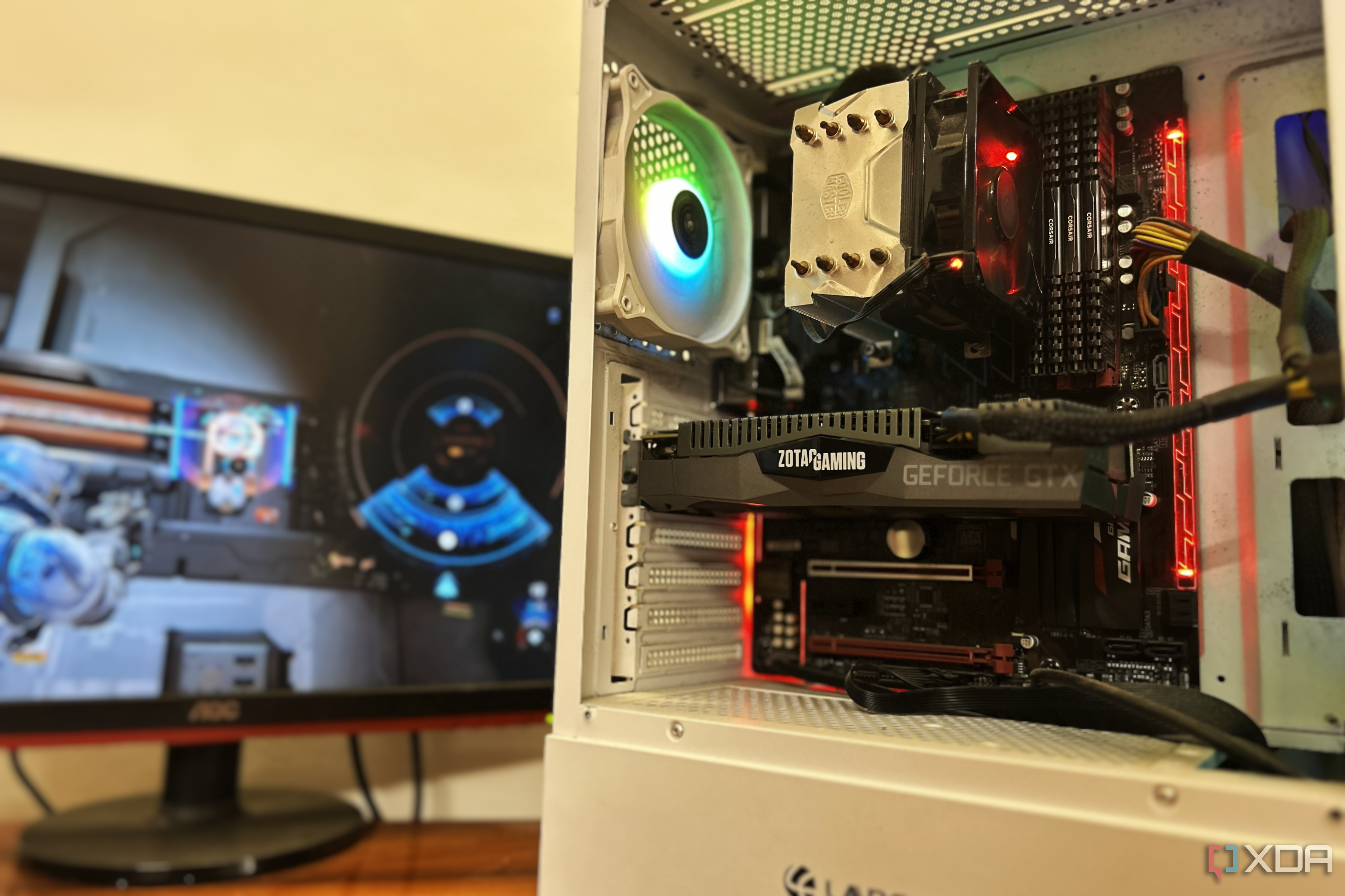 A white gaming PC on a desk with a monitor playing a game in the background