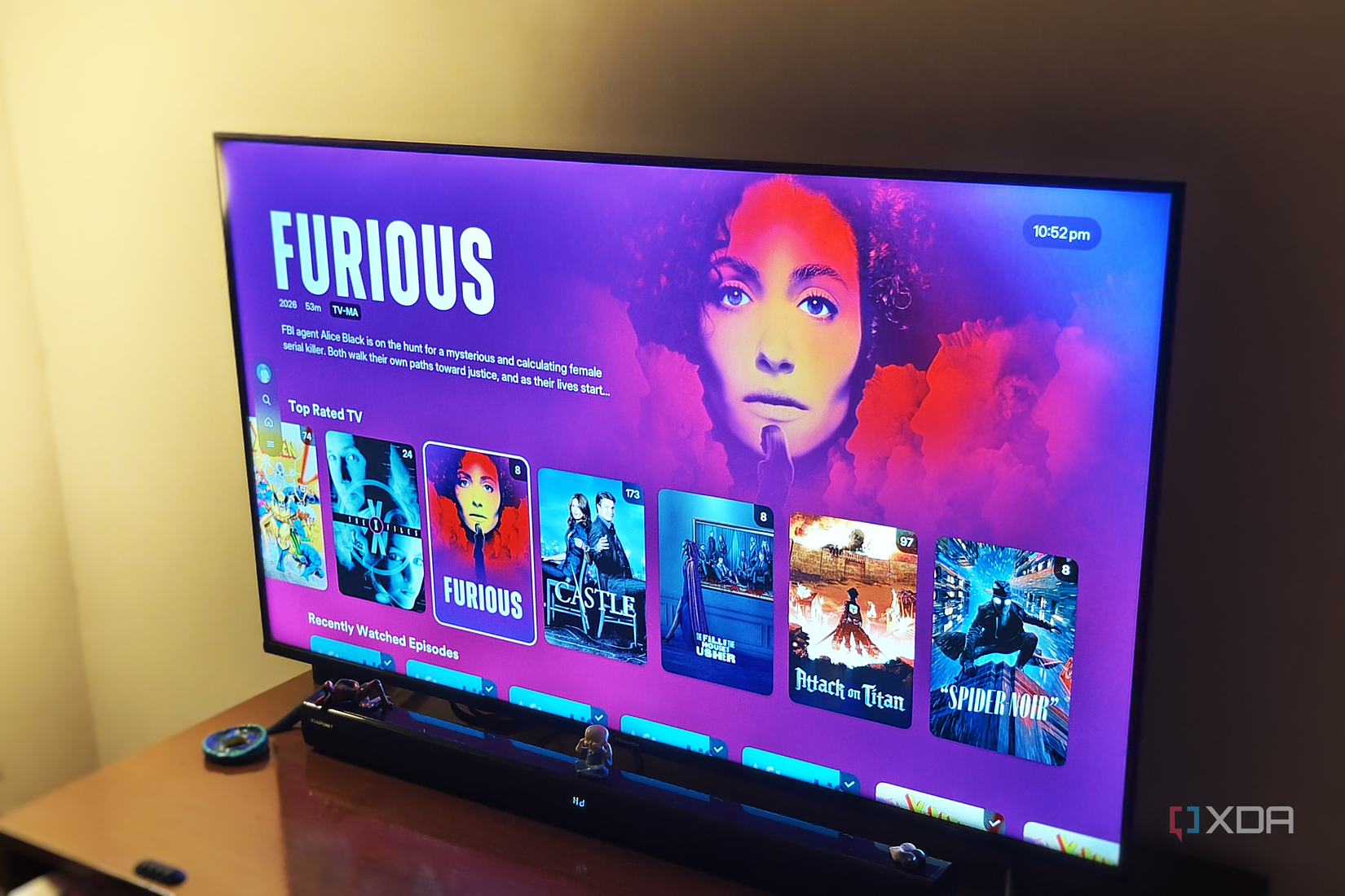 A smart TV on a brown desk in low light showing a list of TV shows on the screen