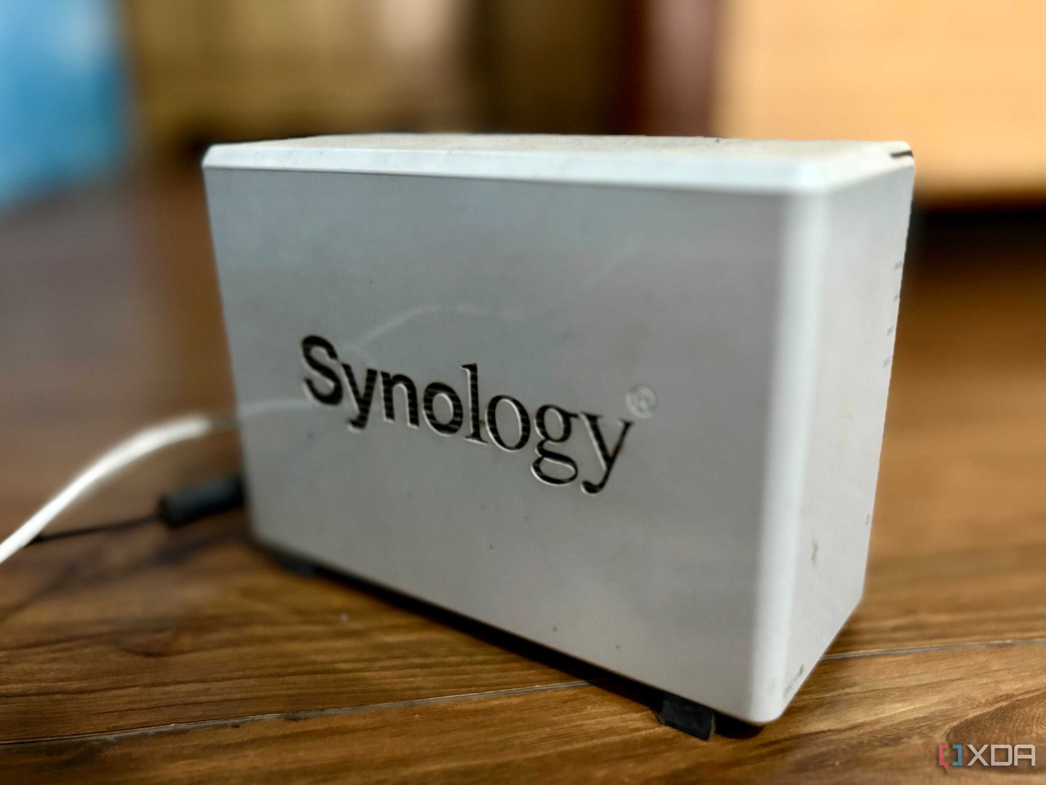 A white two-bay Synology NAS sitting on a wooden desk with its power cable attached