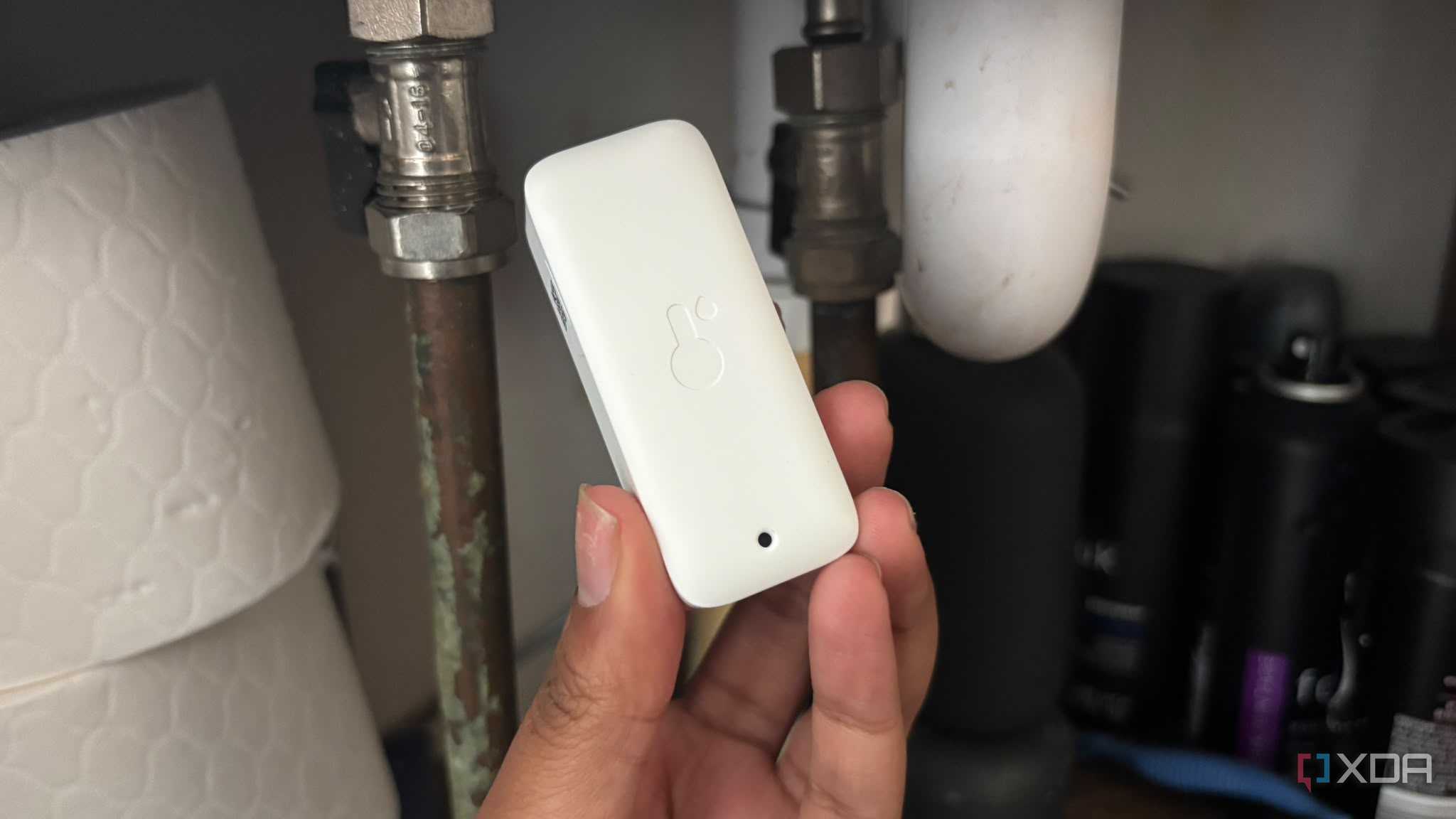 water sensor being held up in front of pipes under sink in cupboard