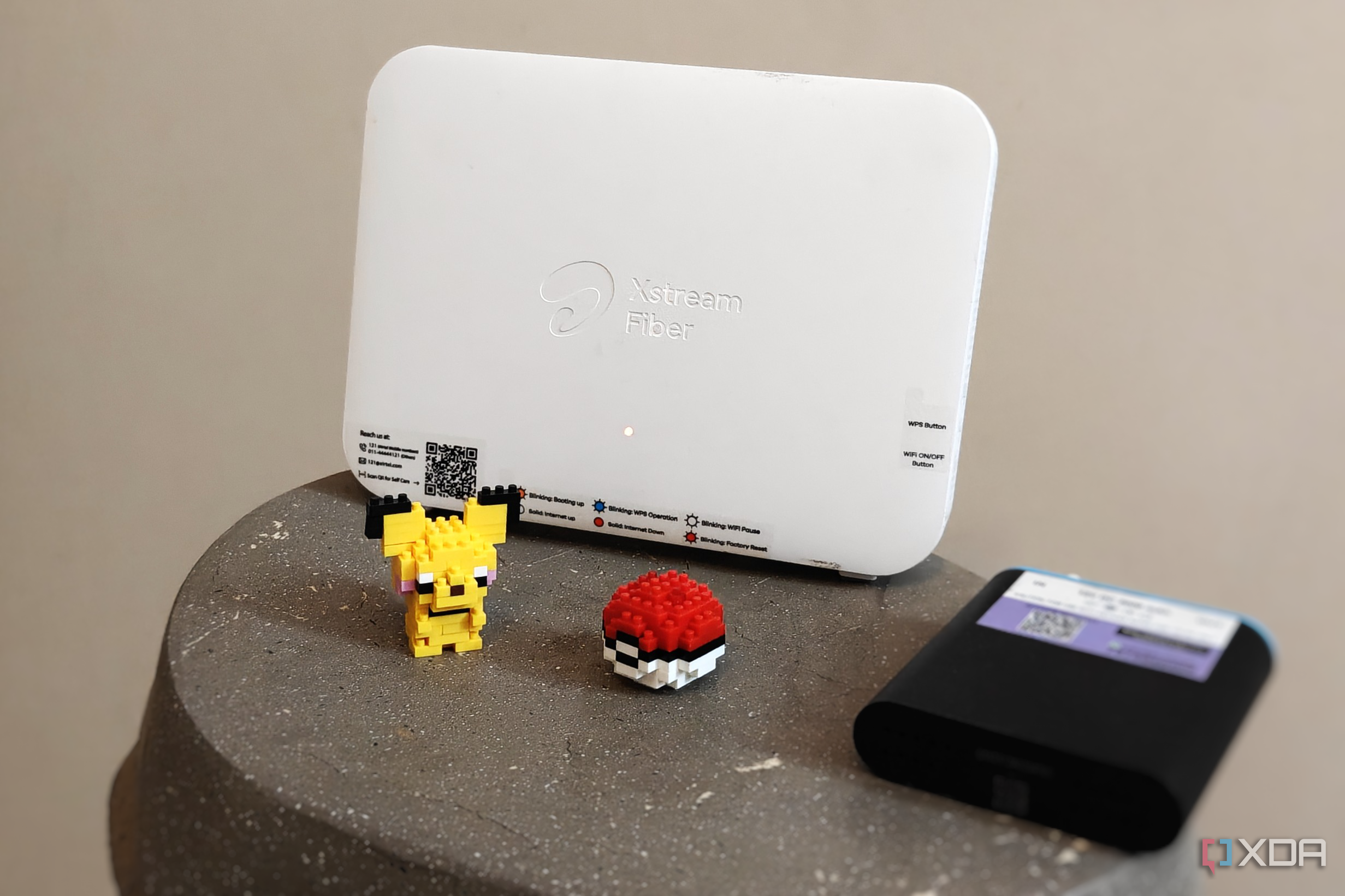 Close-up of a white Wi-Fi router next to a black mini UPS and a Pikachu figurine